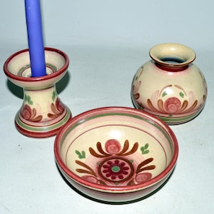 May include: A ceramic candle holder with a blue candle, a small vase, and a bowl. The items are cream-colored with red, green, and brown floral patterns. The bowl and vase have a similar design.