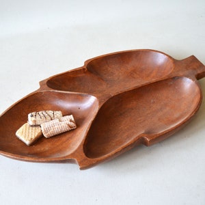 May include: A wooden leaf-shaped serving tray with three compartments. The tray is a warm brown color and contains several small, rectangular cookies. The tray is likely used for serving snacks or appetizers.
