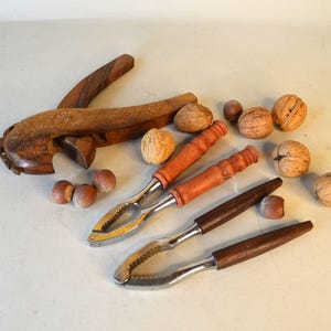 Peut inclure: Deux casse-noix en bois et un tas de noix. Un casse-noix est un modèle en bois traditionnel avec une poignée sculptée. L'autre casse-noix est un modèle plus moderne avec un levier en métal. Les noix sont un mélange de noix et de noisettes.