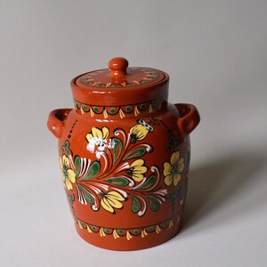 May include: A terracotta jar with a lid, decorated with hand-painted yellow flowers and green leaves on a red background.