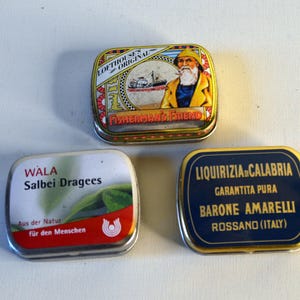 May include: Three small, rectangular metal tins. One tin features a sailor illustration and the text "LOFTHOUSES ORIGINAL FISHERMAN'S FRIEND". Another tin has "WALA Salbei Dragees" with German text. The third tin displays "LIQUIRIZIA CALABRIA" and "BARONE AMARELLI".