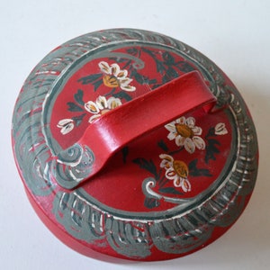 Peut inclure: Couvercle en bois rouge avec un motif floral peint et une poignée. Le couvercle présente un motif floral gris et blanc avec une poignée rouge.