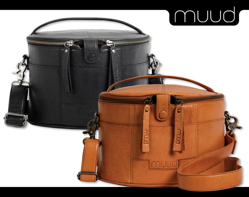 May include: Two leather bucket bags with a top handle and a shoulder strap. The bag on the left is black and the bag on the right is brown. Both bags have a zipper closure and the brand name "muud" is embossed on the front.