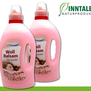 Puede incluir: Dos botellas rosas de suavizante para lana con una etiqueta que dice "Woll Balsam mit Lanolin". Las botellas están sobre un fondo blanco.