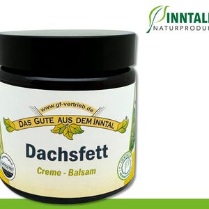 May include: A white jar with a black lid and a green label. The label says "Dachsfett Creme - Balsam" and "Das Gute Aus Dem Inntal".