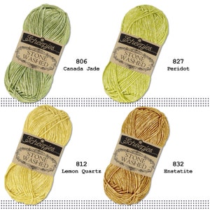 K&ouml;nnte beinhalten: Vier Kn&auml;uel Scheepjes Stone Washed Garn in verschiedenen Farben: Canada Jade, Peridot, Zitronenquarz und Enstatit. Jedes Kn&auml;uel hat ein Etikett mit dem Markennamen und der Garnart.