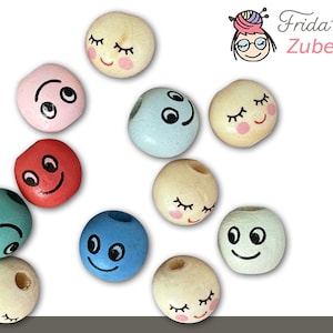 May include: Assortment of wooden beads with painted faces. The beads feature different expressions, including smiling, winking, and sleeping faces. The beads are in various colors, including pink, blue, red, green, and beige.