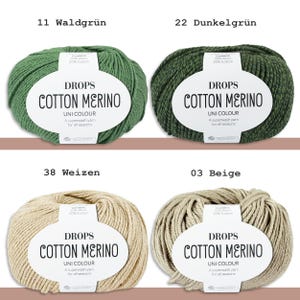 May include: Four skeins of Drops Cotton Merino yarn in various colors: green, dark green, beige, and light beige. Each skein has a white label with the yarn name and details. The text "Cotton Merino" is prominently displayed.