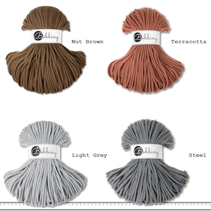 May include: Four skeins of Bobbiny cord in nut brown, terracotta, light grey, and steel colors. Each skein is wrapped in a white paper band featuring the Bobbiny logo. The cord is arranged in a fan-like shape, displaying the texture of the material.