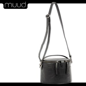 May include: A black leather cylindrical crossbody bag with a top handle and a zipper closure. The bag has a textured leather finish and a silver-toned hardware.