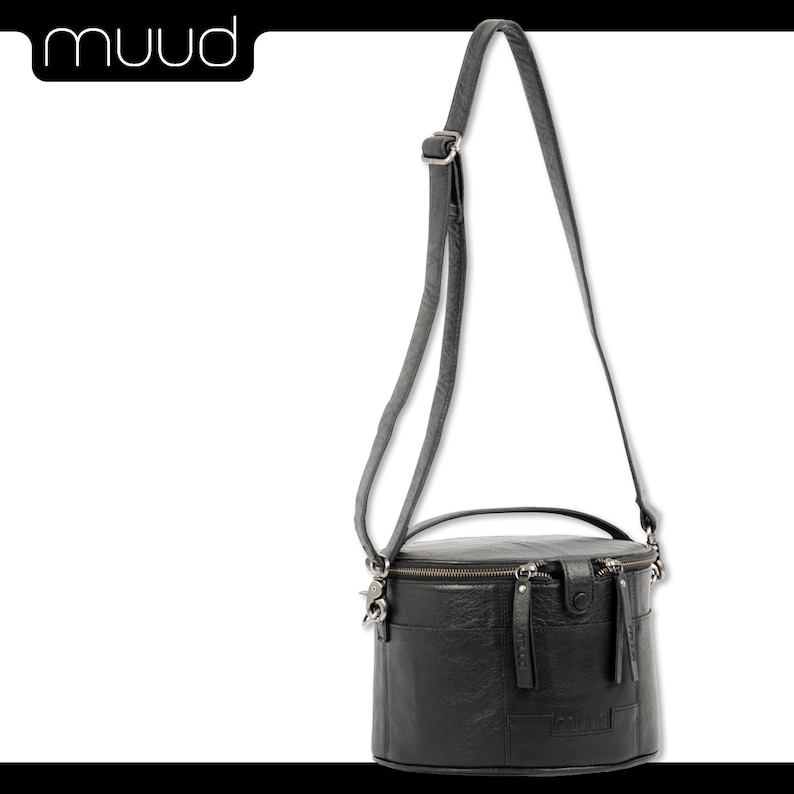 May include: A black leather cylindrical crossbody bag with a top handle and a zipper closure. The bag has a textured leather finish and a silver-toned hardware.