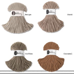K&ouml;nnte beinhalten: Vier Str&auml;nge aus Bobbiny-Baumwollkordel in einem Raster angeordnet, jeder mit einer wei&szlig;en Papierbanderole mit dem Text Bobbiny versehen. Die Farben sind als Beige, Sand, Coffee und Caramel gekennzeichnet und zeigen verschiedene Braun- und Beiget&ouml;ne.