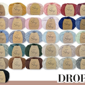 Peut inclure: Une collection de 36 pelotes de laine de différentes couleurs, dont le blanc, le beige, le brun, le rose, le bleu, le vert et le gris. Chaque pelote porte une étiquette sur laquelle est inscrit "DROPS Sky" en blanc.