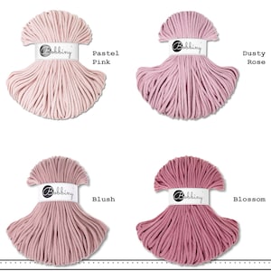 May include: Four skeins of Bobbiny cotton cord arranged in a grid. Each skein features a white paper band with the brand name Bobbiny. The colors are labeled as Pastel Pink, Dusty Rose, Blush, and Blossom, showing varying shades of pink.