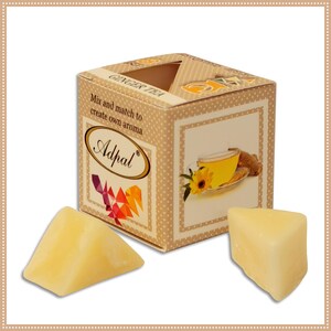 Puede incluir: Una caja de fundentes de cera Adpal de té de jengibre. La caja es marrón con una imagen de una taza de té y un trozo de jengibre. La caja dice "Mix and match to create your own aroma". Hay dos fundentes de cera triangulares en la imagen.