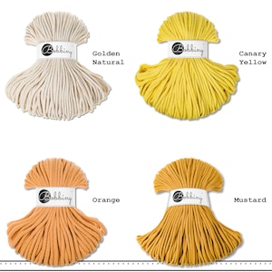 May include: Four skeins of Bobbiny cotton cord arranged in a grid. The colors are labeled as Golden Natural, Canary Yellow, Orange, and Mustard. Each skein is secured with a white paper band featuring the Bobbiny logo in black script text.