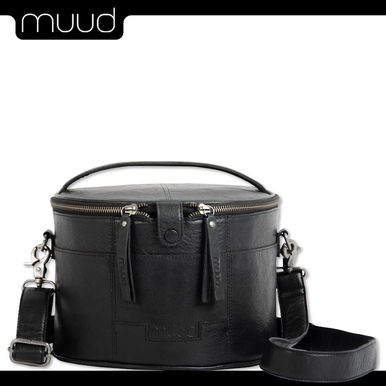 May include: Black leather cylindrical handbag with a top handle and a long adjustable shoulder strap. The bag has two zipper closures and the brand name "muud" is embossed on the front.