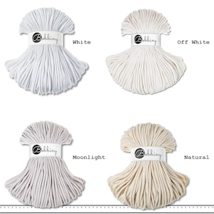 May include: Four bundles of Bobbiny cord arranged in a grid. The colors are labeled as White, Off White, Moonlight, and Natural. Each bundle is secured with a white paper band featuring the Bobbiny logo, showcasing a smooth, braided texture.