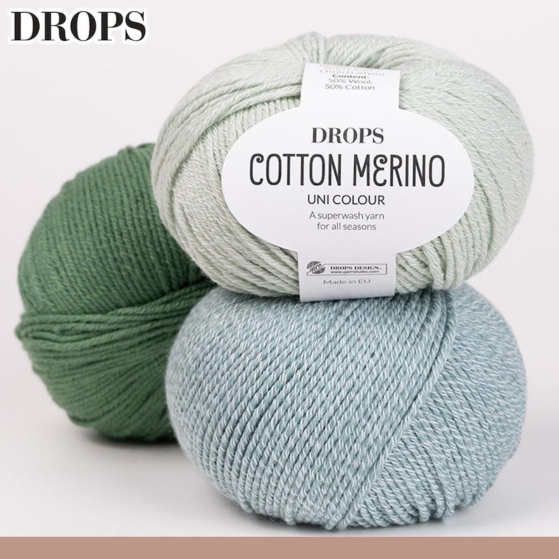 May include: Three balls of DROPS Cotton Merino yarn in shades of green and blue. The center ball has a label that reads "Cotton Merino Uni Colour" and "A superwash yarn for all seasons."