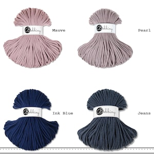 May include: Four skeins of Bobbiny cord arranged in a grid. The top left is mauve, top right is pearl, bottom left is ink blue, and bottom right is jeans. Each skein features a white paper band with the brand name Bobbiny printed in black text.