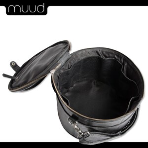 May include: Black leather round travel bag with a zipper closure and a handle. The bag is open and the inside is lined with black fabric.