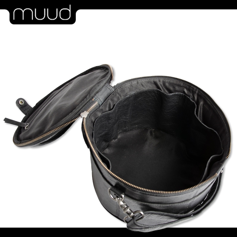 May include: Black leather round travel bag with a zipper closure and a handle. The bag is open and the inside is lined with black fabric.