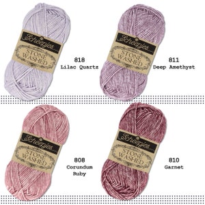K&ouml;nnte beinhalten: Vier Kn&auml;uel Scheepjes Stone Washed Garn in verschiedenen Farben: Lila Quarz, Dunkel Amethyst, Korund Rubin und Granat. Jedes Kn&auml;uel hat ein Etikett mit dem Markennamen und der Garnart.