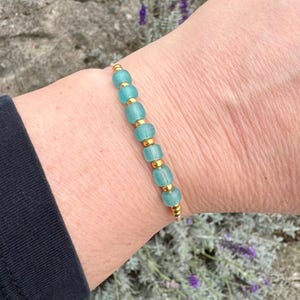 Könnte beinhalten: Ein Armband mit hellblauen Glasperlen und goldenen Akzenten auf einer weißen Schnur.