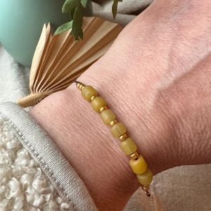 Könnte beinhalten: Ein Armband mit gelb-grünen Perlen und kleinen goldfarbenen Abstandshaltern. Das Armband wird am Handgelenk getragen, vor einem neutralen Hintergrund. Die Perlen haben eine leicht unregelmäßige Form. Das Armband ist ein Schmuckstück.