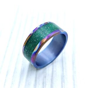 Op de afbeelding: Een groene en blauwe ring met een glinsterende groene band. De ring is gemaakt van metaal en heeft een gepolijste afwerking.