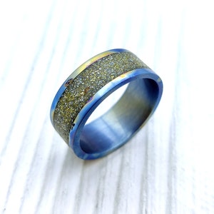 Op de afbeelding: Een blauwe titanium ring met een band van goudkleurige metaalvlokken.