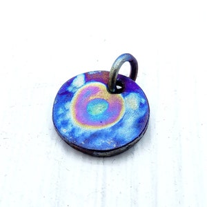 May include: A round, iridescent blue, purple, and gold metal pendant with a silver loop at the top.
