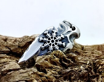 May include: A silver-colored pendant shaped like an arrowhead, featuring a snowflake design in the center. The pendant has a textured surface and is displayed on a piece of wood. The snowflake is intricately detailed.