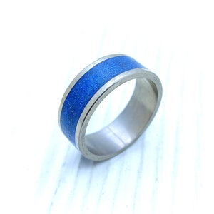 Op de afbeelding: Een zilveren ring met een blauwe inlay. De inlay heeft een gespikkelde textuur.