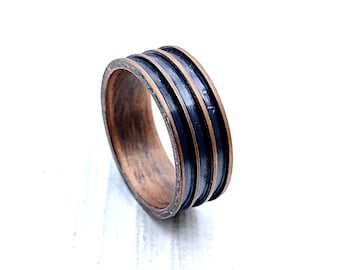 May include: A copper and black wood ring with three black stripes around the band.
