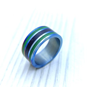 Op de afbeelding: Een blauwe titanium ring met groene en zwarte strepen.