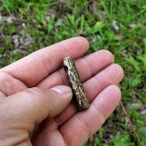 May include: A small, hammered brass tube with a hole through the center. The tube is about 2 inches long and has a rough, textured surface.