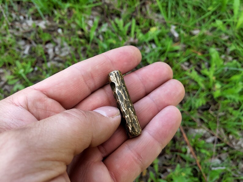 May include: A small, hammered brass tube with a hole through the center. The tube is about 2 inches long and has a rough, textured surface.