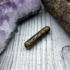 May include: A hammered brass pendant with a textured surface. The pendant is a long, thin cylinder shape with rounded ends.