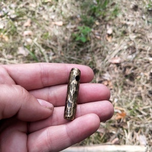 May include: A small, hammered brass cylinder with a hole through the center. The cylinder is about 2 inches long and has a textured surface.