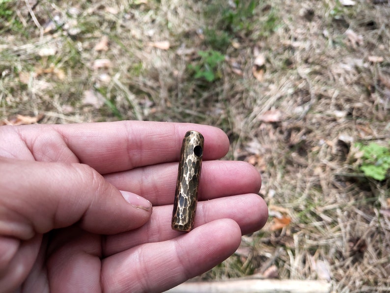 May include: A small, hammered brass cylinder with a hole through the center. The cylinder is about 2 inches long and has a textured surface.