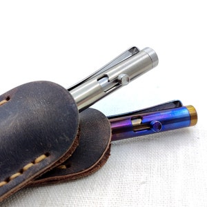 May include: Two titanium pens in a brown leather case. One pen is silver and the other is blue and purple.
