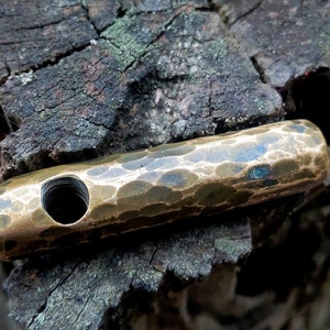 May include: A hammered brass pendant with a hole in the center. The pendant has a textured surface and a dark patina.
