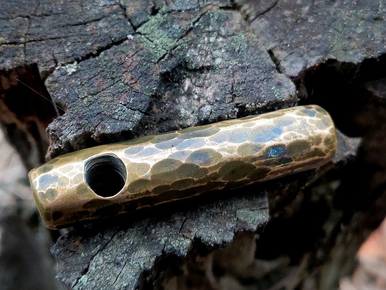 May include: A hammered brass pendant with a hole in the center. The pendant has a textured surface and a dark patina.