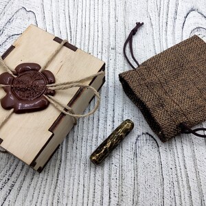 May include: A wooden box with a brown wax seal and a brown burlap pouch with a gold metal stamp inside.