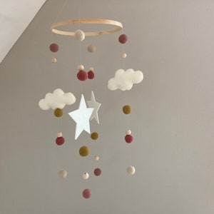 Könnte beinhalten: Ein weißes und braunes Filz-Babymobil mit Wolken, Sternen und Bommeln, die an einem Holzring hängen.