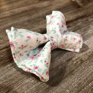 May include: A white bow tie with a pink and green floral pattern.