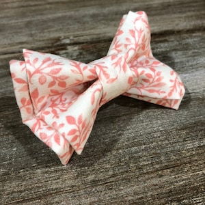 May include: A pink and white bow tie with a floral pattern. The bow tie is made of fabric and has a classic shape.