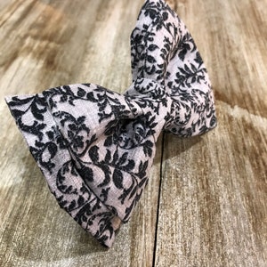 May include: A gray bow tie with a black floral pattern.