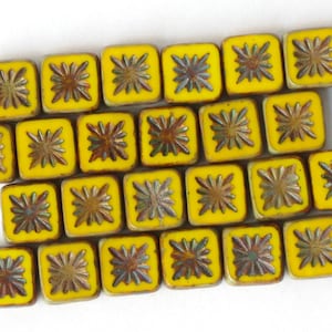 Può includere: Una collezione di piastrelle quadrate in ceramica gialle con un motivo a stella in rilievo di colore marrone scuro. Le piastrelle sono disposte in file e hanno una finitura lucida.